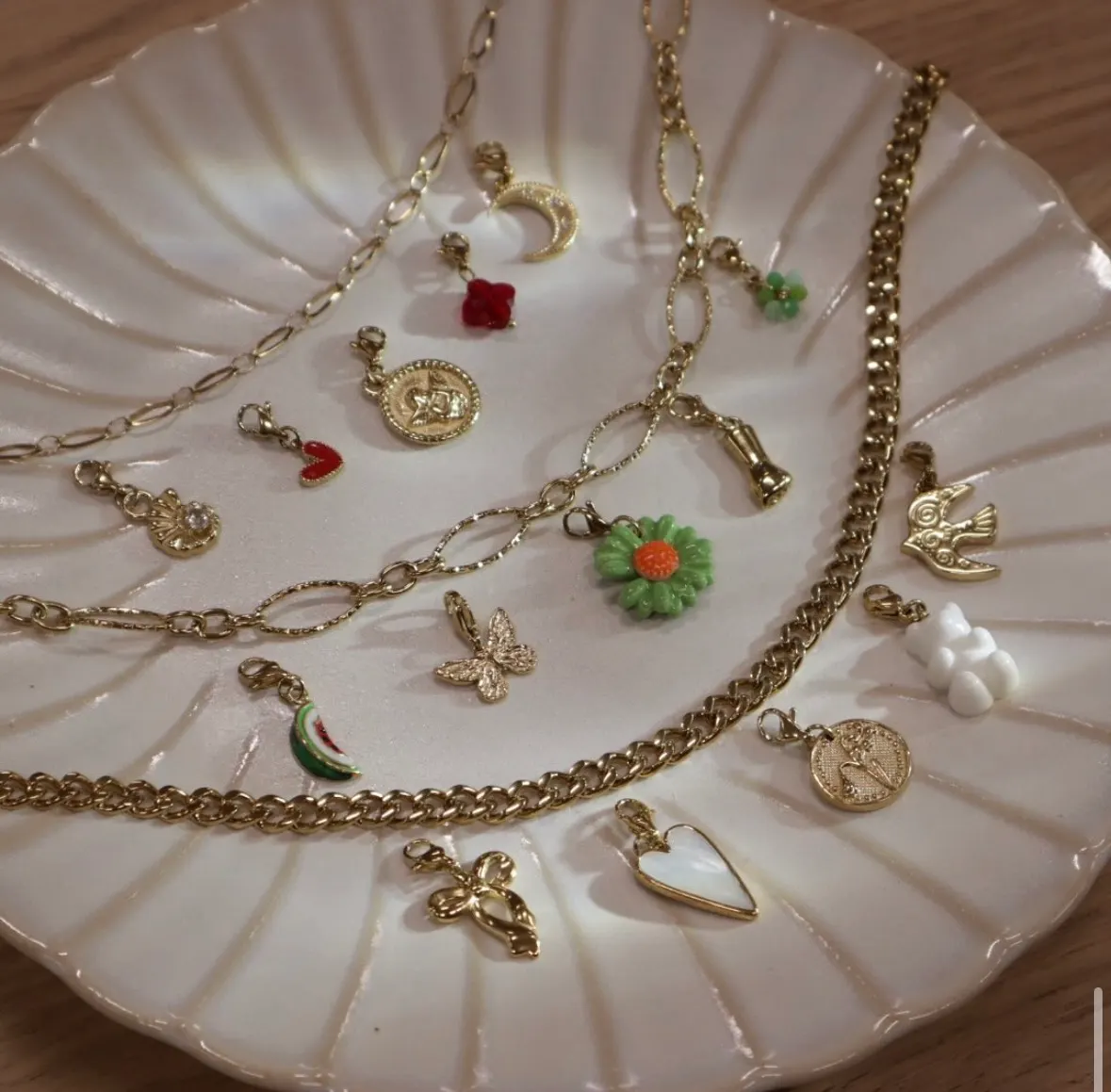 Chaînes dorées et nuée de charms colorés posés sur une assiette nacrée